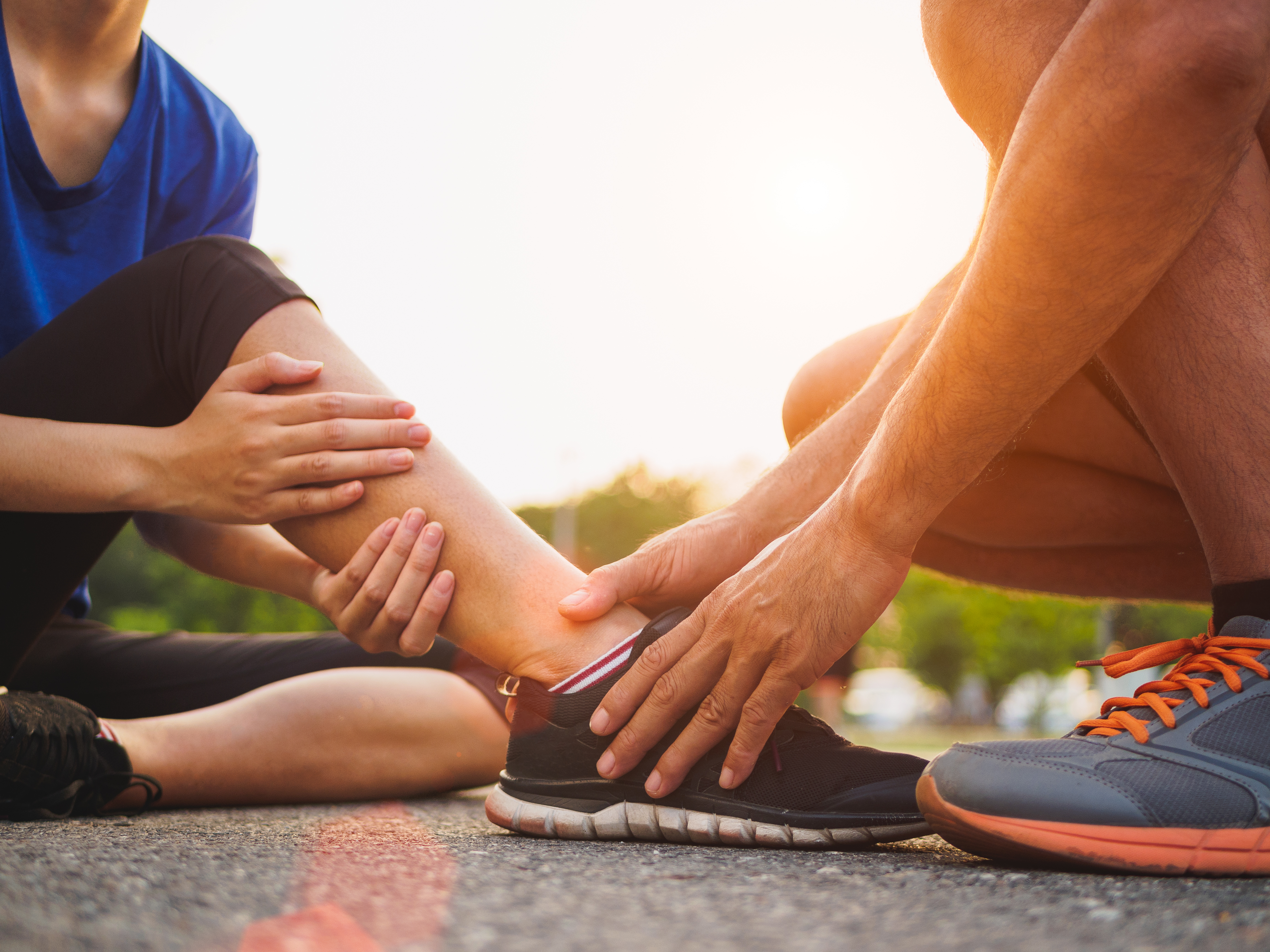 Ankle sprained. Young woman suffering from an ankle injury while exercising and running and she getting help from man touching her ankle. Healthcare and sport concept.