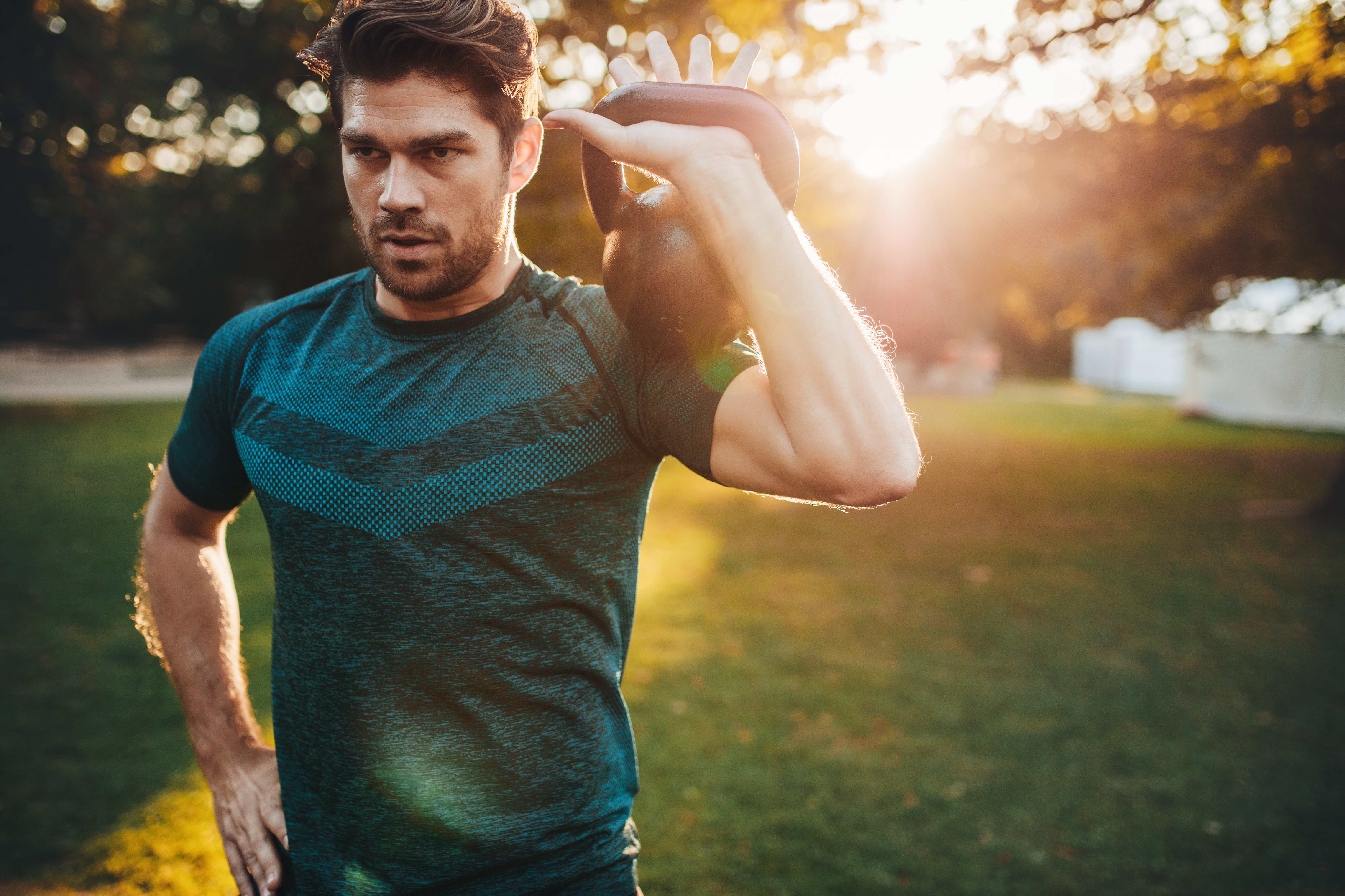 Shot of fit young man exercising with kettlebell in the park.  Strong young guy training at park in morning.