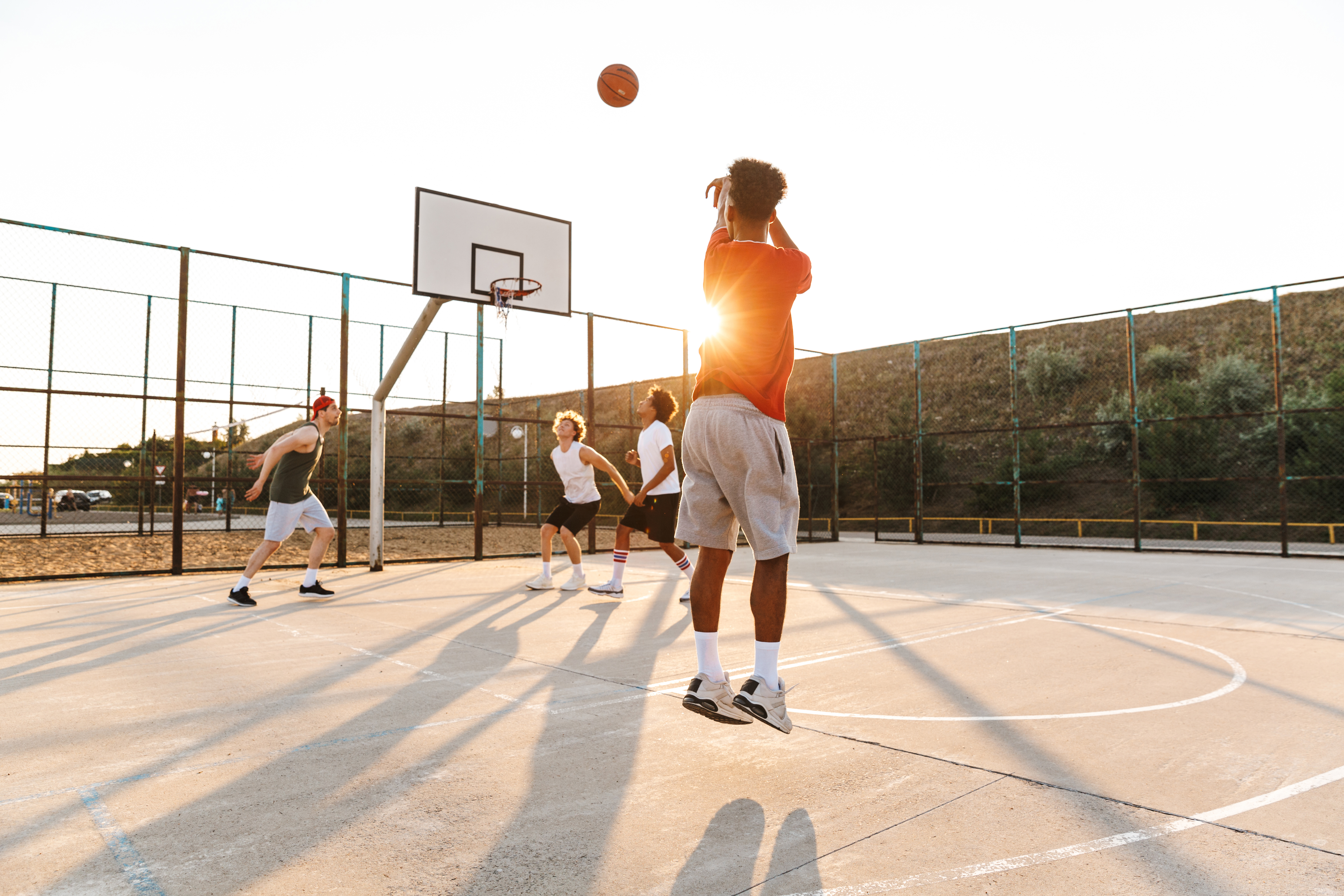 Group of young cheerful multiethnic men basketball players playing basketball at the sport ground, sunrise