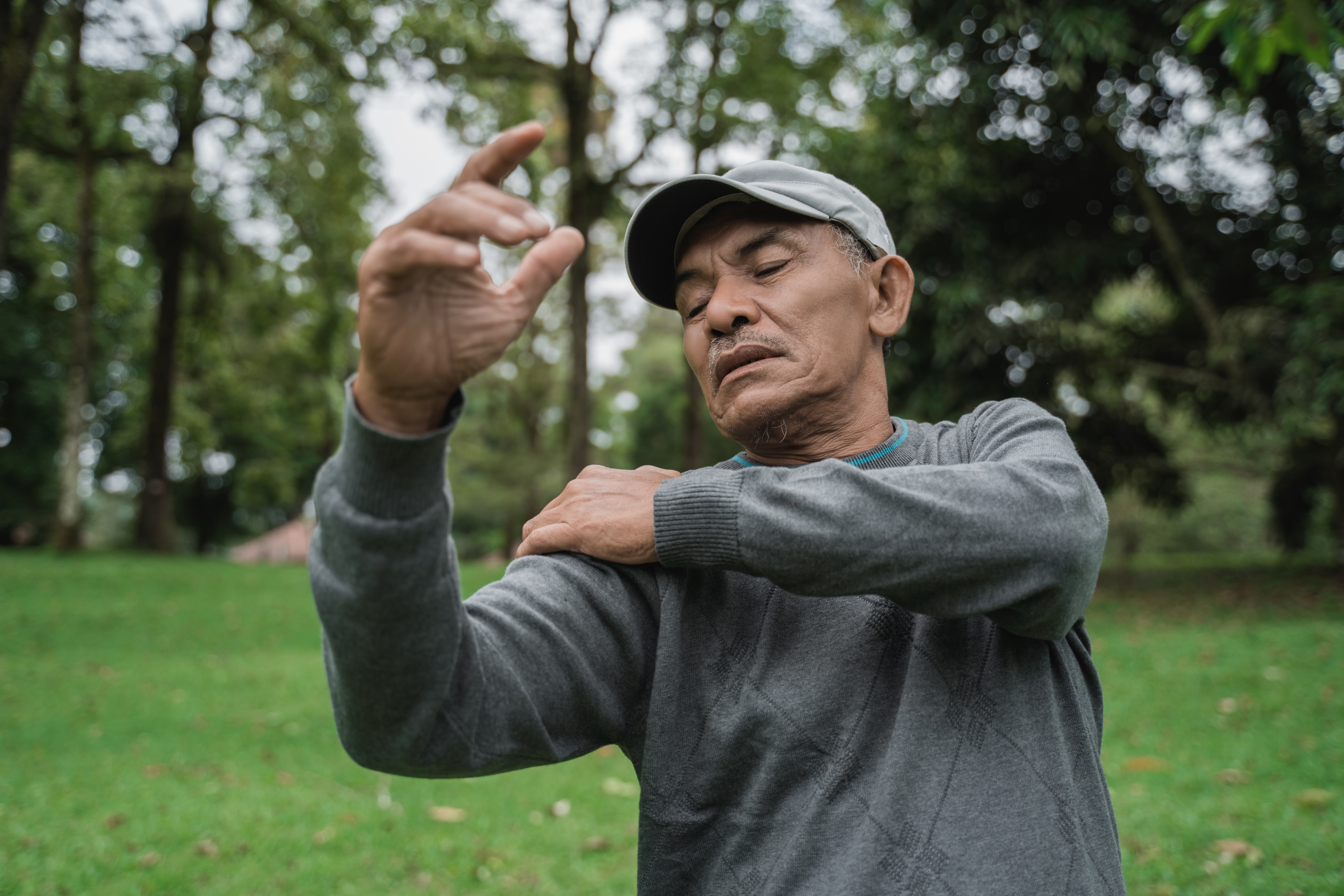 senior male asian having sore shoulder and pain on his joint while relaxing in the park