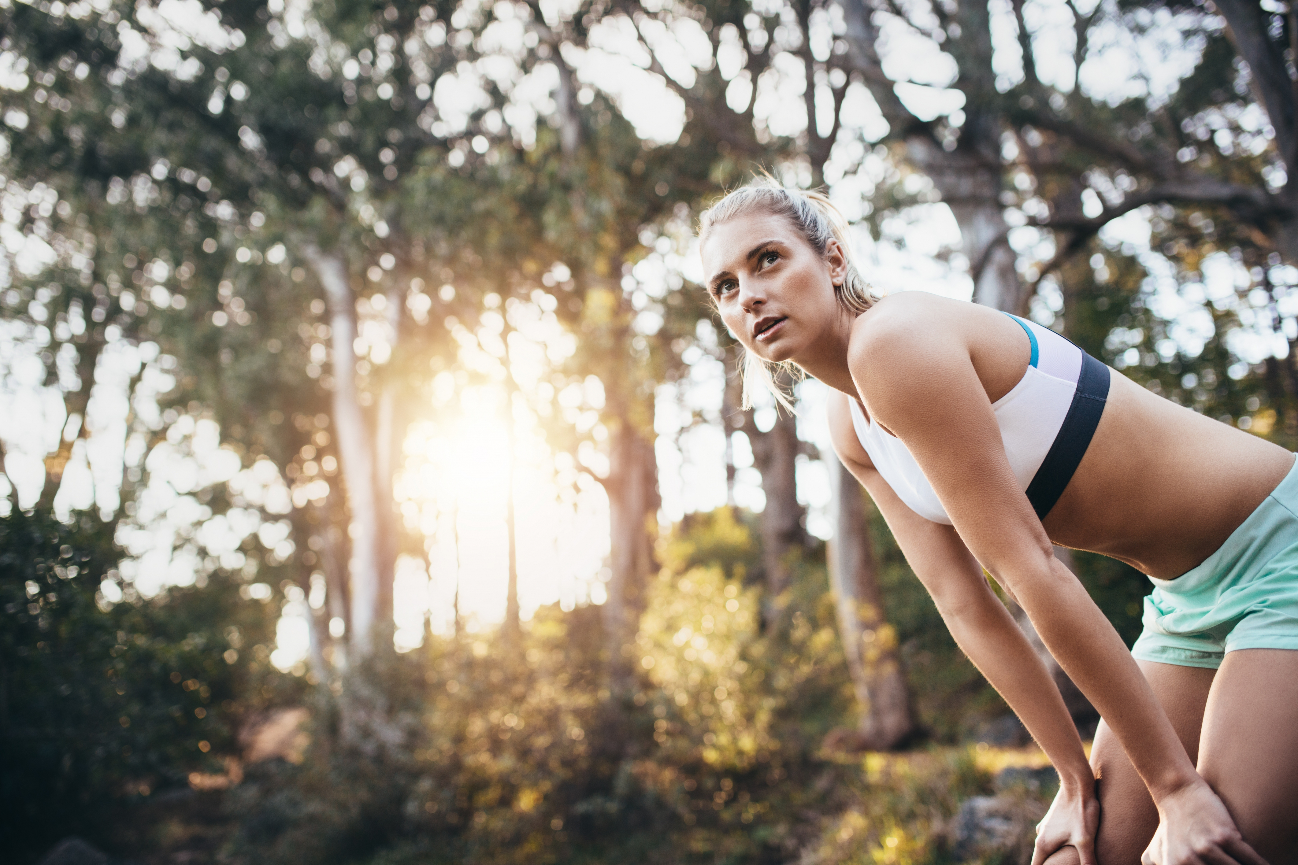 Female athlete relaxing after a run. Woman taking a break from exercise and relaxing with hands resting on knees in a park.